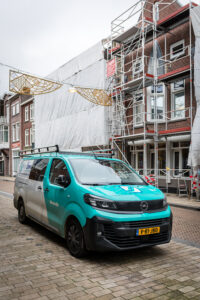 Bedrijfsbus van Van Son Onderhoud en Renovatie bij appartementencomplex in steigers in Tilburg